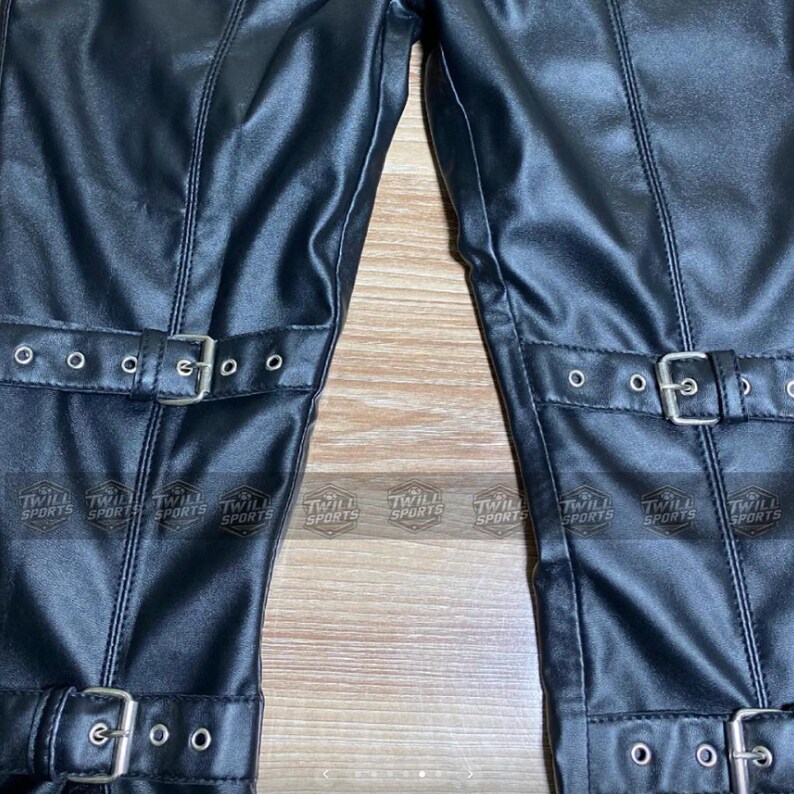 Puede incluir: Primer plano de pantalones de cuero negro con hebillas y correas plateadas. Los pantalones tienen un aspecto texturizado y costuras visibles. Las palabras "TWILL SPORTS" est&aacute;n impresas en una etiqueta.