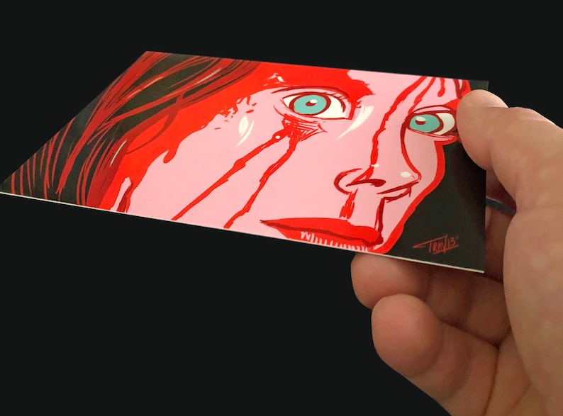 May include: A close-up of a woman's face with red paint dripping down her cheeks. Her eyes are wide open and her expression is one of fear. The background is black.