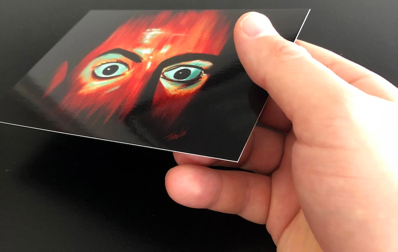 May include: Close-up of a person's face with red and orange skin tones. The person has large, wide-set eyes with green irises. The image is painted in a stylized, almost abstract style.