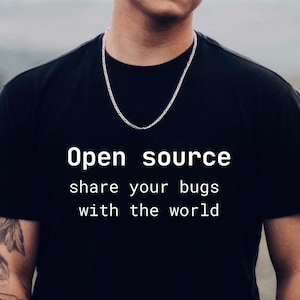 以下が含まれることがあります： 「Open source share your bugs with the world」の白い文字が入った黒いTシャツ。シルバーのチェーンネックレスが見えます。Tシャツはクルーネックです。