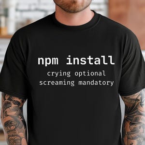 Può includere: T-shirt nero con la scritta bianca "npm install", seguita da "crying optional" e "screaming mandatory". La maglietta ha un design girocollo.