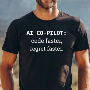 May include: Black t-shirt with the text "AI CO-PILOT: code faster, regret faster" in white. The shirt is a crew neck style and is being worn by a person.