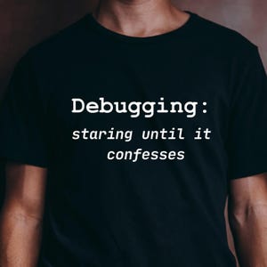Puede incluir: Camiseta negra con el texto blanco "Debugging: staring until it confesses". La camiseta es de cuello redondo y parece estar hecha de un material suave. El texto está centrado en la parte delantera de la camiseta.