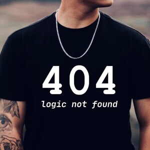 May include: Black t-shirt featuring the number "404" in white, with the words "logic not found" underneath. A silver chain necklace is worn. The shirt is on a person.