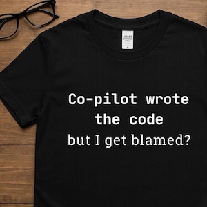 Könnte beinhalten: Schwarzes T-Shirt mit dem weißen Text "Co-pilot wrote the code but I get blamed?". Das Shirt hat einen Rundhalsausschnitt und kurze Ärmel. Das Shirt besteht aus einem weichen Material.