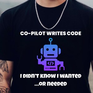 Può includere: T-shirt nera con la scritta "CO-PILOT WRITES CODE" sopra una grafica di un robot viola e blu. Sotto, il testo recita "I DIDN'T KNOW I WANTED...OR NEEDED". La persona indossa una collana a catena d'argento.