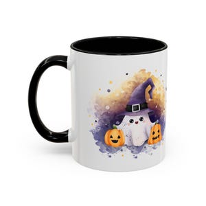 Peut inclure: Mug en céramique blanche avec une anse et un intérieur noirs. L'illustration représente un fantôme portant un chapeau de sorcière violet, avec deux citrouilles orange. Le design a un thème d'Halloween.