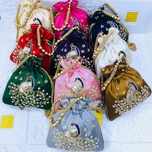 May include: A collection of colorful drawstring bags. Each bag features a peacock design with gold and silver embroidery. The bags come in various colors, including red, green, pink, blue, and gold, with gold beaded handles.