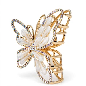 May include: A gold-toned metal hair claw clip shaped like a butterfly. The wings are outlined with iridescent rhinestones and feature white, pearlescent, petal-shaped accents in the center. The clip has a functional spring-loaded mechanism.