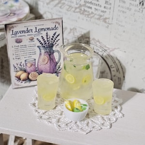 May include: A miniature set featuring a clear glass pitcher and two glasses filled with yellow lemonade and lemon slices, a small white bowl of lemon wedges, and a rectangular sign labeled Lavender Lemonade.