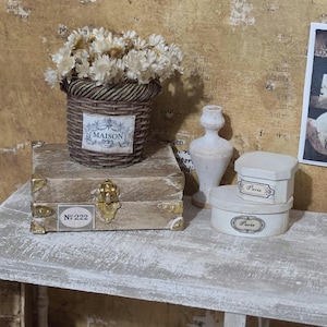 May include: A miniature decorative scene featuring a woven basket with dried flowers, a small wooden chest, and two small white boxes labeled "Paris." The basket has a "MAISON" label. The chest has "Nº 222" on it.