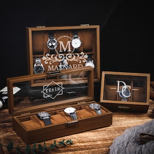 Może przedstawiać: Drewniane gabloty na zegarki ze szklanymi pokrywami. Gabloty są brązowe z beżowymi wnętrzami i mieszczą wiele zegarków. Jedna gablota ma wygrawerowane na szkle imię "MAYWARD" i literę "M".