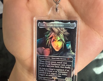 Könnte beinhalten: Ein klarer Acryl-Schlüsselanhänger mit einer Magic: The Gathering-Karte mit der Figur Cloud, Midgar Mercenary. Die Kartenkunst zeigt eine männliche Figur mit stacheligen blonden Haaren. Der Kartentext ist sichtbar.