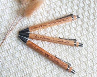 Puede incluir: Tres bolígrafos de bambú con clips y puntas de metal plateado. Cada bolígrafo está grabado con nombres y fechas: Anne et Robin 29 Aout 2026, Marie & Maxime 25 Juillet 2026 y Marie & Maxime 25 Juillet 2026 con un icono de corazón.