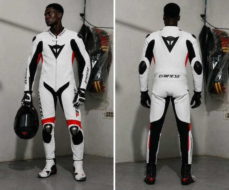 May include: White and black motorcycle racing suit with red accents. The suit features the Dainese logo and is worn with black gloves and boots. A black helmet is held in one hand. The suit has protective padding on the knees and elbows.