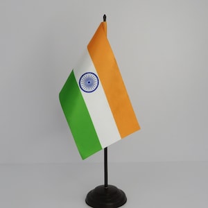 May include: A small Indian flag on a black stand. The flag features horizontal bands of orange, white, and green, with a blue wheel emblem in the center of the white band. The flag is displayed against a plain white background.