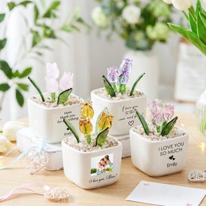 May include: A white ceramic mug with a black handle and the text "But First, Coffee" in a black, handwritten-style font. The mug is on a white surface.