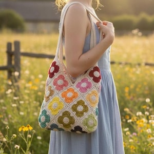 May include: A crocheted tote bag with a floral pattern in various colors, including red, pink, orange, yellow, green, and blue. The bag is carried by a person wearing a light blue dress. The background is a field of wildflowers.