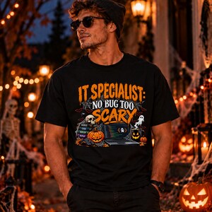 Könnte beinhalten: Ein schwarzes Kurzarm-T-Shirt mit einem Grafikdruck und dem Text IT SPECIALIST: NO BUG TOO SCARY. Das Design zeigt einen Laptop, einen Bücherstapel mit der Aufschrift DEBUG, CODE, DEPLOY, REPEAT, einen Totenkopf, ein Gespenst und einen Kürbis.