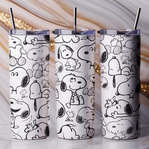 Könnte beinhalten: Drei weiße isolierte Becher mit schwarz-weißen Snoopy-Cartoon-Illustrationen. Jeder Becher hat einen schwarzen Strohhalm und einen durchsichtigen Deckel. Der Hintergrund ist ein Marmormuster mit goldenen Akzenten.
