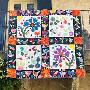 Peut inclure: Une courtepointe faite à la main et colorée, ornée de motifs floraux et d'oiseaux. La courtepointe présente de grandes fleurs bleues et violettes sur fond blanc, entourées de petites fleurs et d'oiseaux. La bordure est noire avec des accents orange et rouges.