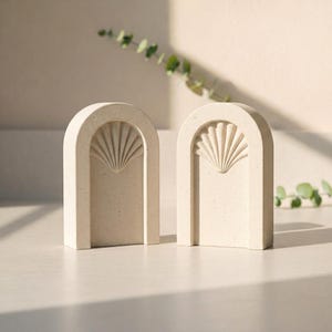 Peut inclure: Deux serre-livres arqués blanc cassé avec une finition texturée. Chaque serre-livre présente un motif en forme d'éventail à l'intérieur de l'arche. Les serre-livres sont faits d'un matériau moucheté et sont exposés sur une surface claire.