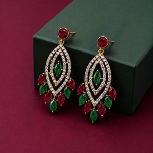 May include: A pair of gold-tone drop earrings featuring a marquise-shaped frame encrusted with clear white crystals. Each earring is accented with a central green marquise stone and a dangling fringe of alternating red and green marquise stones.