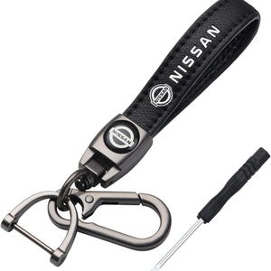 Könnte beinhalten: Schwarzer Leder-Schlüsselanhänger mit dem Wort "NISSAN" in weißer Schrift und dem Nissan-Logo. Der Schlüsselanhänger hat einen Metallverschluss und einen kleinen Schraubendreher.