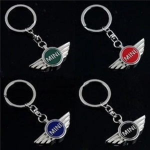 May include: Four MINI keyrings featuring a silver wing design and a circular emblem. The emblems are in green, red, blue, and black, each with the word "MINI" in white. The keyrings have a silver ring.