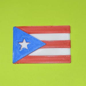May include: A rectangular flag of Puerto Rico, featuring three red stripes, two white stripes, a blue triangle on the hoist side, and a white star in the center of the triangle. The flag is set against a solid green background.