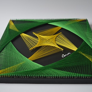 Pode incluir: Uma peça de arte em fio quadrada com fundo preto. O design apresenta uma forma central de estrela amarela, rodeada por fios verdes e amarelos. A assinatura do artista, "Coran", está no canto inferior direito.
