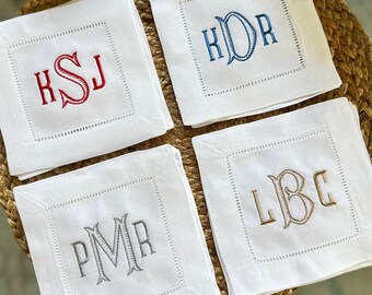 May include: Four white linen napkins with embroidered initials in different colors. The initials are "KSJ", "KDR", "PMR", and "LBC".