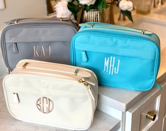 May include: Three toiletry bags with different colored fabric and personalized monograms. The bags are gray, white, and light blue. The monograms are "KAJ", "MHJ", and "BCD".