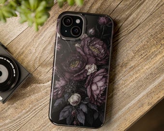 May include: Black phone case featuring a dark floral design with purple and white flowers. The case has a glossy finish and a camera cutout. The phone case is on a wooden surface.