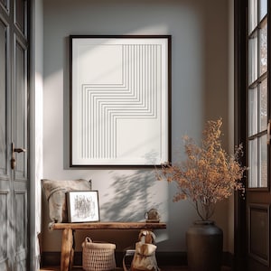 Könnte beinhalten: Ein gerahmter Kunstdruck mit einem schwarz-weißen geometrischen Design hängt an einer Wand. Das Kunstwerk zeigt eine Reihe von vertikalen und horizontalen Linien. Unter dem Kunstwerk befindet sich eine Holzbank mit einem Kissen, einem Korb und einem Rucksack.