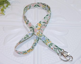 May include: A white lanyard with a floral pattern in shades of pink, yellow, blue, and green. The lanyard has a silver swivel clasp.