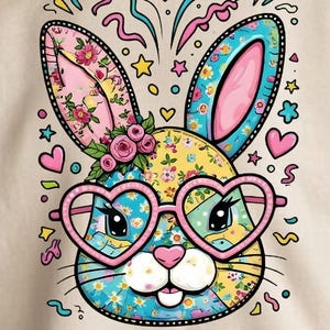 Peut inclure: Un sweat-shirt beige avec un motif de lapin de Pâques coloré. Le lapin porte des lunettes en forme de cœur, des oreilles à motifs floraux et une coiffe florale. Autour du lapin, on trouve des cœurs, des étoiles et des volutes décoratives.