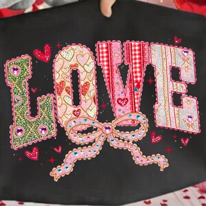 Peut inclure: Coussin décoratif noir avec le mot "LOVE" dans un design coloré et à motifs. Les lettres sont ornées de cœurs, de nœuds et de strass. Le coussin est tenu par une personne.
