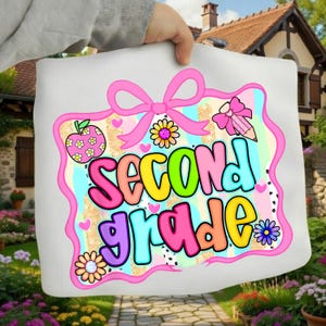 Peut inclure: Une surface en tissu blanc avec un graphique coloré bordé d'un nœud rose. Le texte Second Grade est écrit en lettres bulles multicolores. Le motif inclut des illustrations d'une pomme rose, d'un crayon et de fleurs sur un fond pastel.