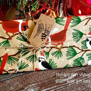 May include: Holiday gift wrap with a bird and branch design in red, green, and white on a tan background. The gift is tied with twine and includes a gift tag with a bird illustration. The text "Holiday Gift Wrap with gift card" is visible.