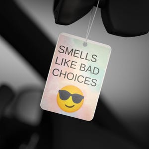 Może przedstawiać: Prostokątna etykieta z napisem "Smells Like Bad Choices" i emotikonem z okularami przeciwsłonecznymi. Etykieta ma akwarelowe tło w pastelowych kolorach. Etykieta wisi na sznurku.