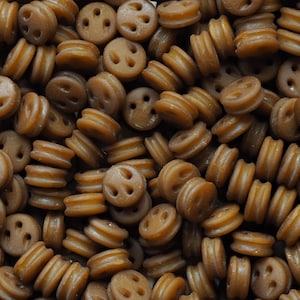 May include: A close-up of a collection of brown smiley face buttons. Each button features a smiley face design with three holes for the eyes and mouth. The buttons are stacked and arranged in a random pattern.