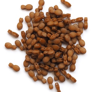 May include: A pile of brown, bean-like objects against a white backdrop. The objects are smooth and glossy, with a consistent colour. The shapes vary, some being more elongated than others. The objects are scattered.
