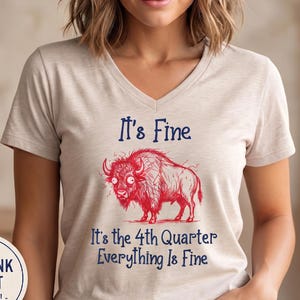 Może przedstawiać: Beżowy t-shirt z dekoltem w serek, ozdobiony czerwoną grafiką liniową przedstawiającą żubra na środku. Tekst nad żubrem brzmi It's Fine, a tekst poniżej It's the 4th Quarter Everything Is Fine, napisany niebieską czcionką.