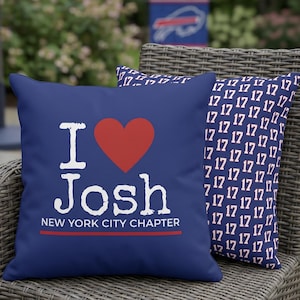 May include: Two navy blue throw pillows on a wicker chair. One pillow has the text "I ❤️ Josh" with "NEW YORK CITY CHAPTER" below. The other pillow has a pattern of the number "17".