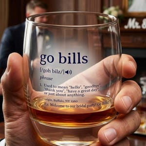 Könnte beinhalten: Ein klares Glas mit dem Aufdruck "go bills", gehalten von einer Person. Das Glas enthält eine braune Flüssigkeit. Der Text enthält eine Definition und den Ursprung.