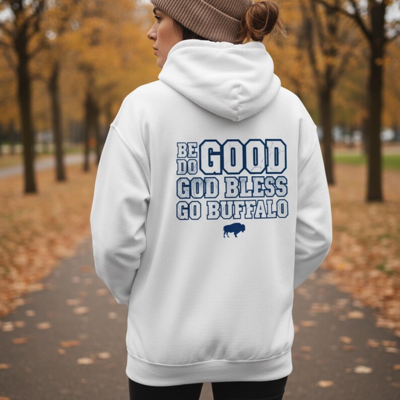 Puede incluir: Sudadera con capucha blanca con cord&oacute;n y mangas largas. La parte trasera de la sudadera tiene el texto "BE GOOD GOD BLESS GO BUFFALO" en azul marino, junto con un gr&aacute;fico de b&uacute;falo. La sudadera con capucha la lleva una persona.