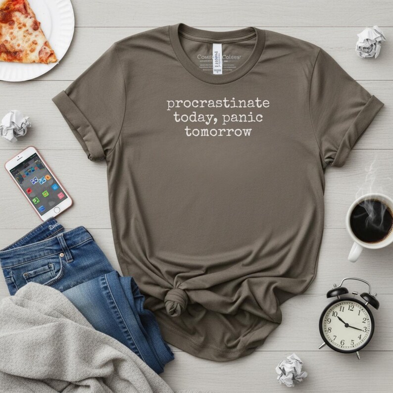 May include: A brown t-shirt with the text "procrastinate today, panic tomorrow" in white. The shirt is knotted at the bottom. Other items include a pair of blue jeans, a smartphone, a cup of coffee, and a black alarm clock.