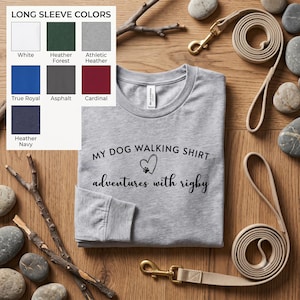 K&ouml;nnte beinhalten: Ein hellgraues Langarmshirt mit schwarzem Text, der MY DOG WALKING SHIRT lautet, einem Herzsymbol mit Pfotenabdruck und dem Text adventures with rigby. Eine Farbkarte zeigt die Optionen Wei&szlig;, Heather Forest, Athletic Heather, True Royal, Asphalt, Cardinal und Heather Navy.