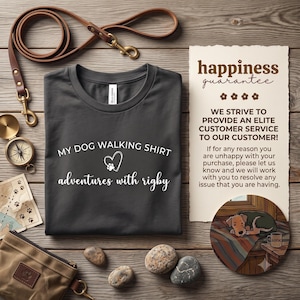 K&ouml;nnte beinhalten: Ein dunkelgraues T-Shirt mit dem wei&szlig;en Text MY DOG WALKING SHIRT und adventures with rigby sowie einem Herz- und Pfotenabdruck-Symbol. Das T-Shirt wird zusammen mit einer braunen Lederleine, einem Kompass, einer Karte, einem Beutel und einer Karte gezeigt.